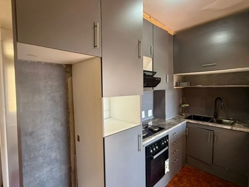 A compact kitchen featuring grey cabinetry, built-in oven, hob, and double sink, currently requiring finishing touches to wall surfaces and trim.