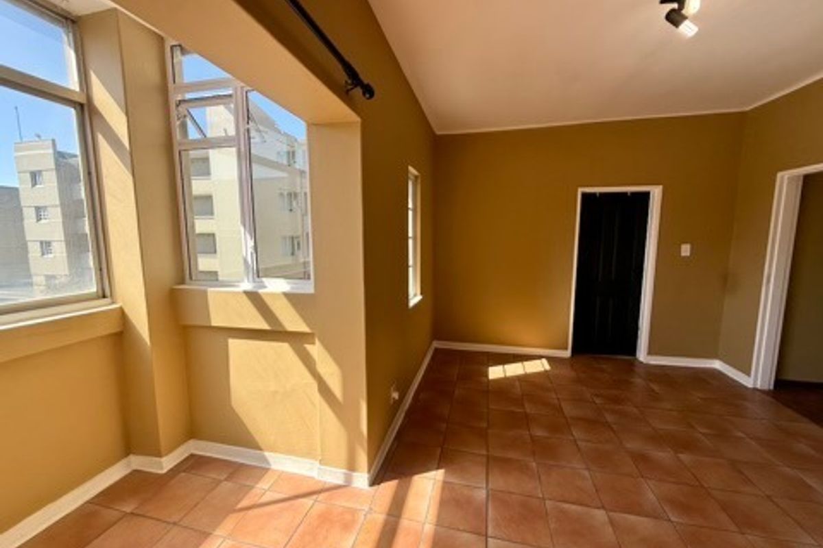 A bright, empty living area featuring tiled flooring, large windows providing natural light, and modern track lighting.