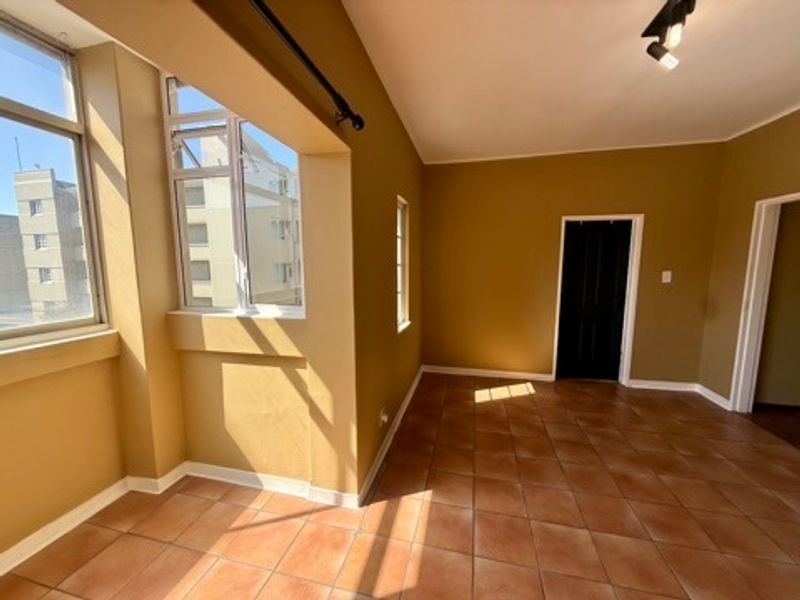 A bright, empty living area featuring tiled flooring, large windows providing natural light, and modern track lighting.