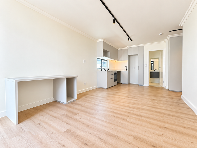 Modern open-plan living area featuring light wood-look flooring, sleek built-in cabinetry, integrated kitchen appliances, and a dedicated built-in desk space.