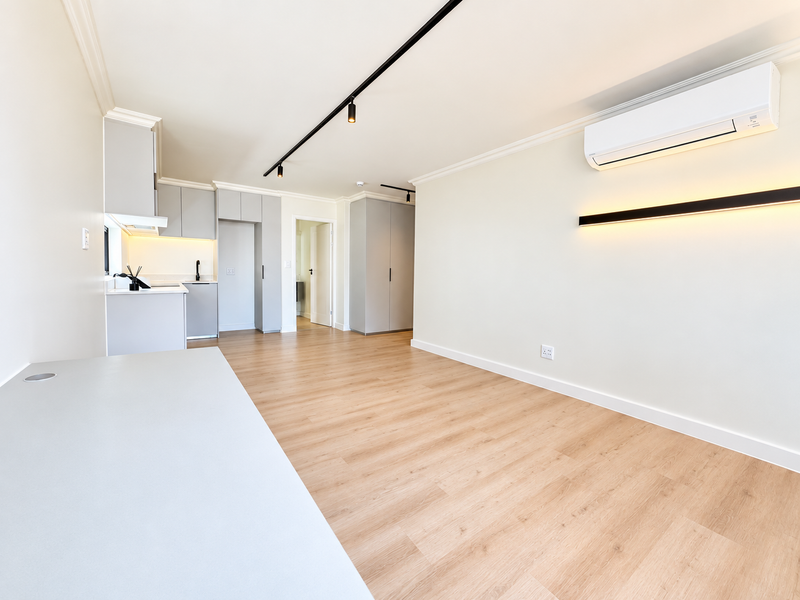 Modern open-plan living area featuring light laminate flooring, sleek built-in cabinetry, track lighting, and a wall-mounted air conditioning unit.
