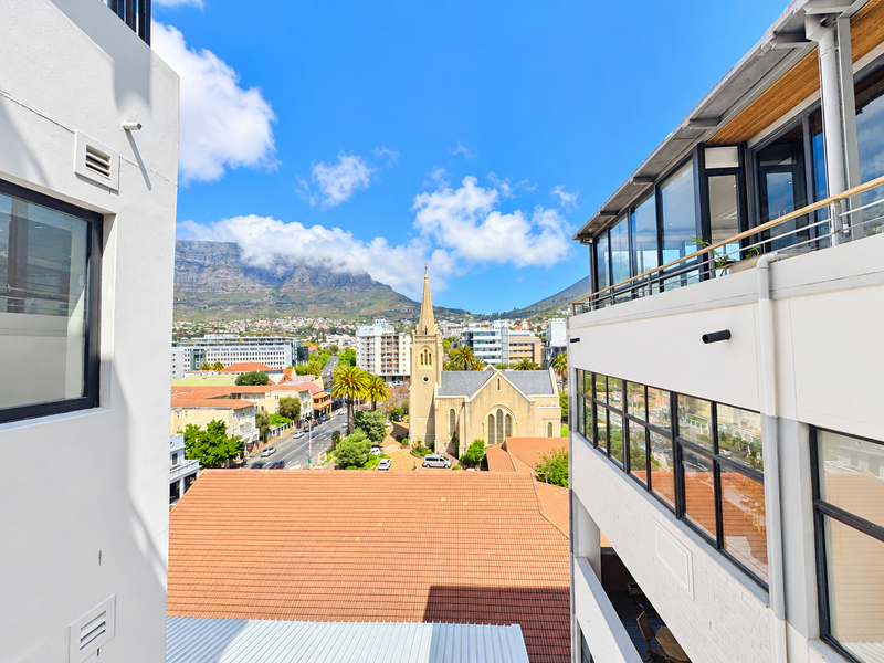 A scenic urban view featuring a historic church, surrounding city architecture, and a prominent mountain backdrop, framed by modern apartment building facades.
