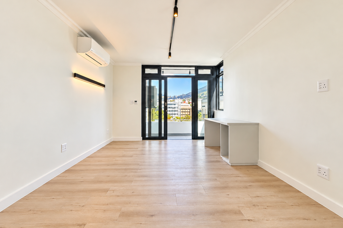 Bright and modern living area featuring light laminate flooring, air conditioning, track lighting, and sliding glass doors leading to a balcony with city views.