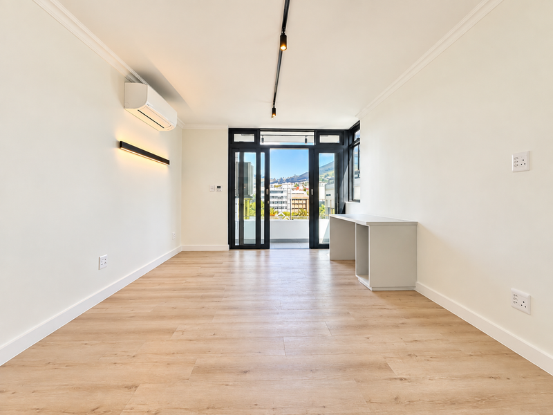Bright and modern living area featuring light laminate flooring, air conditioning, track lighting, and sliding glass doors leading to a balcony with city views.