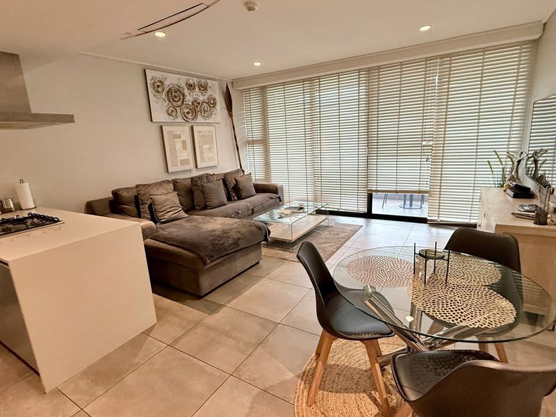 Modern open-plan living area featuring a sleek kitchen with gas hob, tiled floors, and large sliding doors leading to a balcony.