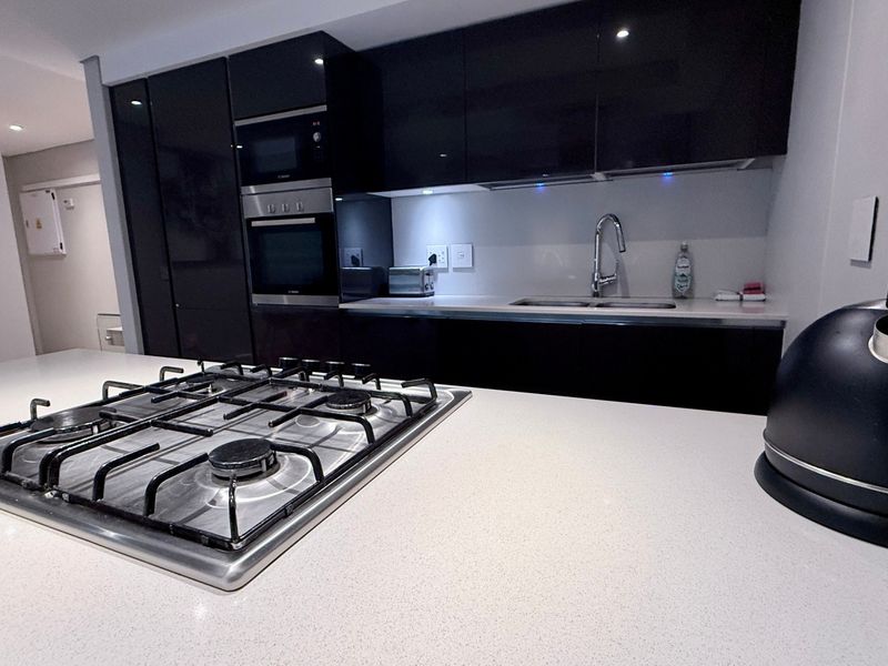 Modern kitchen featuring high-gloss cabinetry, stone countertops, a gas cooktop, and integrated appliances, offering a sleek and functional culinary space.