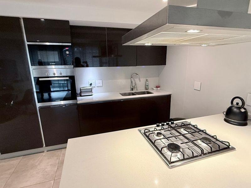 Modern kitchen featuring dark cabinetry, stone countertops, a central island with a gas hob, built-in oven, and integrated extractor fan.