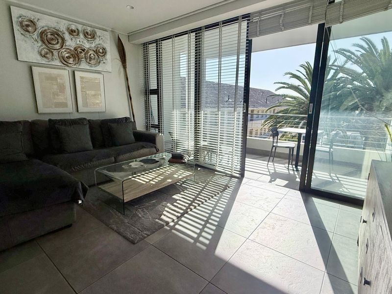 A bright living room featuring large sliding glass doors that open onto a balcony, complemented by modern tiled flooring and recessed lighting.