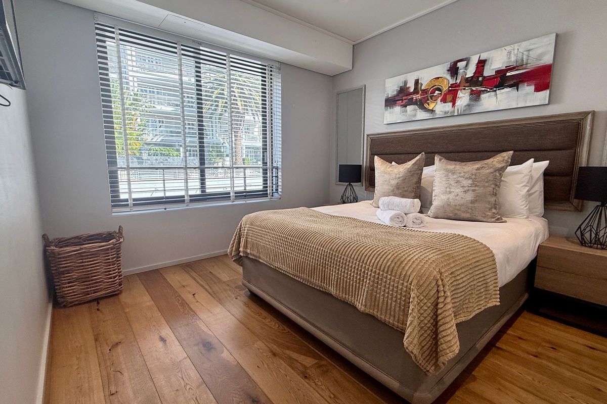 A well-maintained bedroom featuring warm hardwood flooring, a built-in headboard, and venetian blinds allowing natural light.