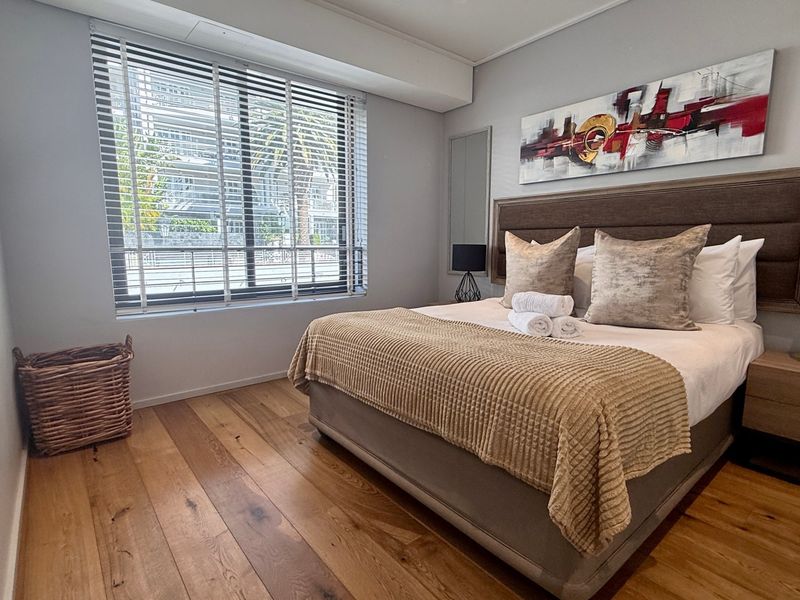 A well-maintained bedroom featuring warm hardwood flooring, a built-in headboard, and venetian blinds allowing natural light.