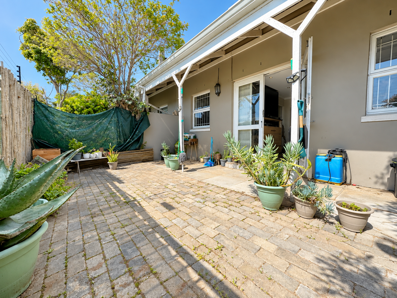 A paved outdoor patio area featuring a covered veranda, sliding door access, and established garden borders, offering a functional space for outdoor living.