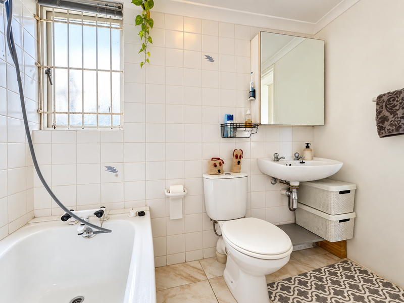 A functional bathroom featuring a bathtub, pedestal sink, toilet, and wall-mounted mirror cabinet, finished with white wall tiles and neutral floor tiles.