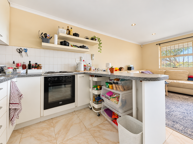 Open-plan kitchen featuring white cabinetry, built-in oven, hob, and tiled splashback, seamlessly flowing into the adjacent living area.