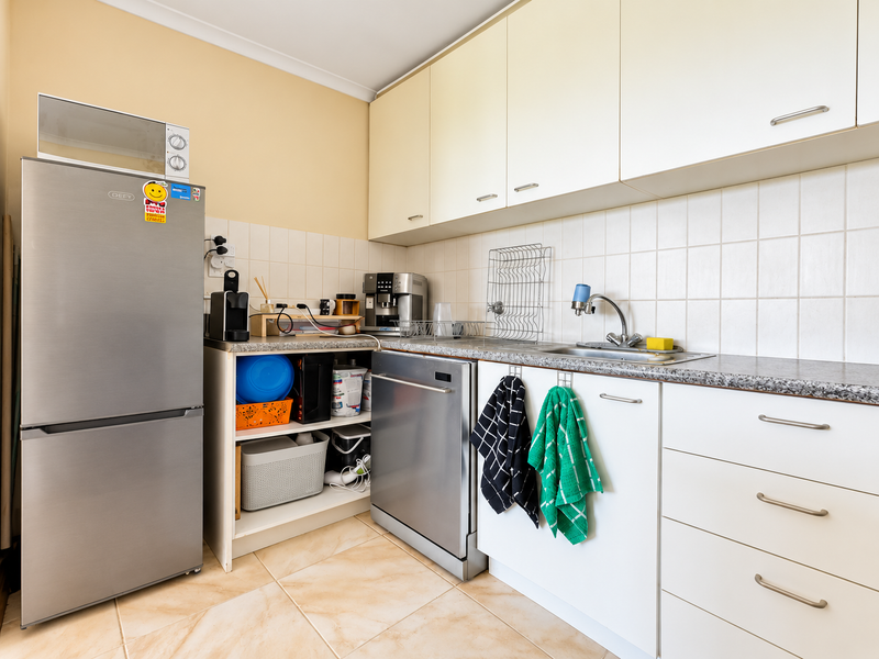 A functional kitchen featuring white cabinetry, laminate countertops, tiled backsplash, and integrated dishwasher, providing a practical workspace with neutral finishes.