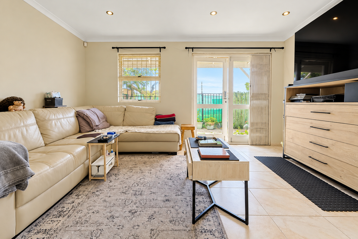 A bright living room featuring tiled flooring, recessed downlights, and direct access to an outdoor area through a sliding glass door with a security gate.
