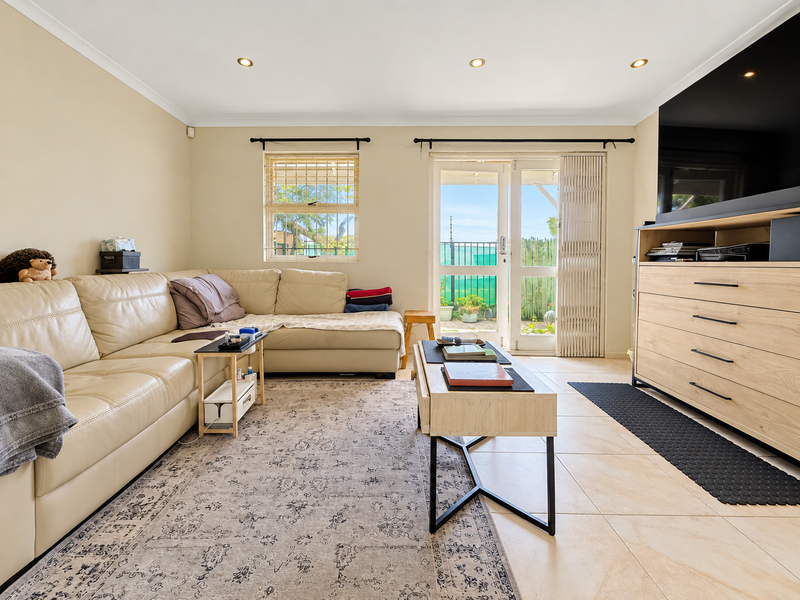 A bright living room featuring tiled flooring, recessed downlights, and direct access to an outdoor area through a sliding glass door with a security gate.