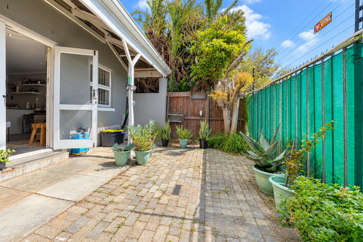 A private rear courtyard featuring paved flooring, timber fencing, and a green privacy screen, providing direct access to the interior living space.