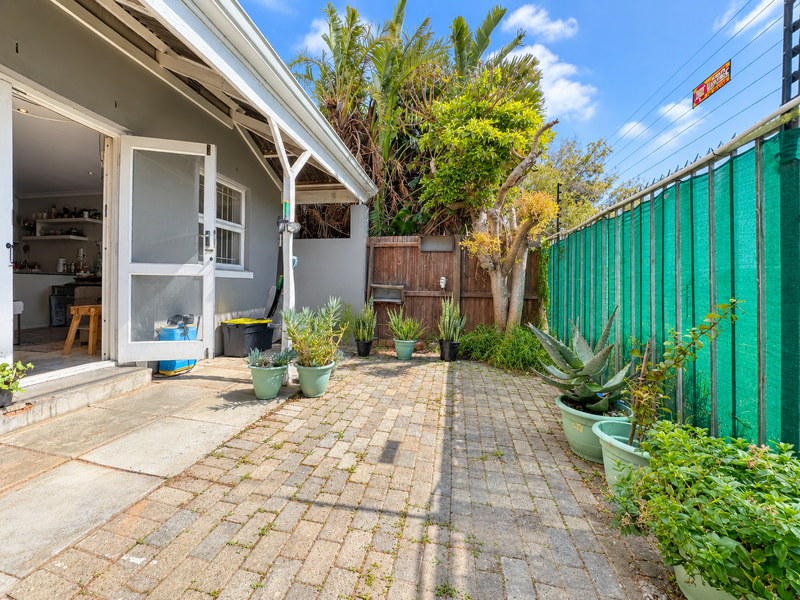 A private rear courtyard featuring paved flooring, timber fencing, and a green privacy screen, providing direct access to the interior living space.