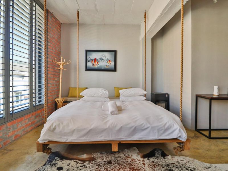 A modern industrial-style bedroom featuring exposed brick walls, polished concrete flooring, and a unique suspended bed frame.