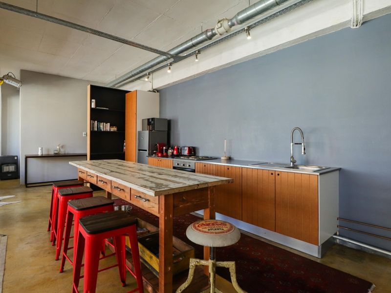 Industrial-style kitchen featuring exposed ceiling ducting, wooden cabinetry, stainless steel sink, and a central wooden island in an open-plan apartment setting.