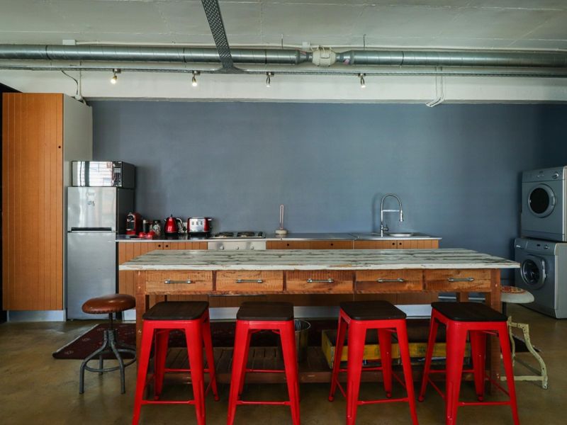 Open-plan kitchen area featuring industrial-style exposed ceiling ducting, concrete flooring, and integrated laundry appliances, offering a functional and modern urban aesthetic.