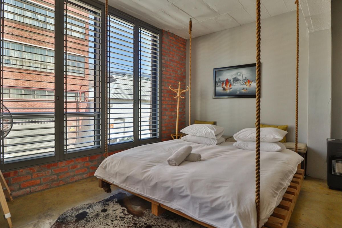 A modern industrial-style bedroom featuring exposed brick walls, polished concrete floors, and large windows that provide ample natural light.