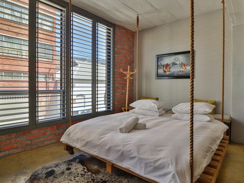 A modern industrial-style bedroom featuring exposed brick walls, polished concrete floors, and large windows that provide ample natural light.