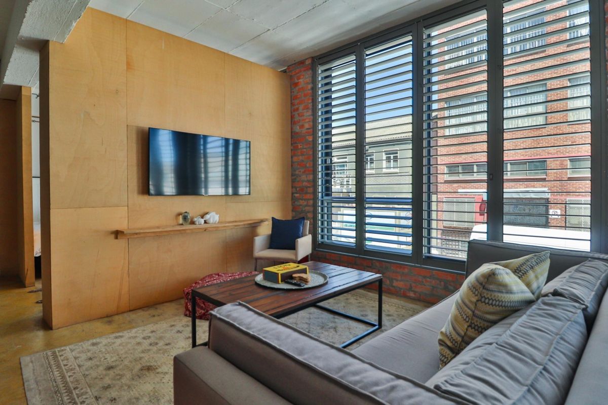 Modern industrial-style living room featuring exposed brick walls, plywood paneling, polished concrete floors, and large windows providing ample natural light.