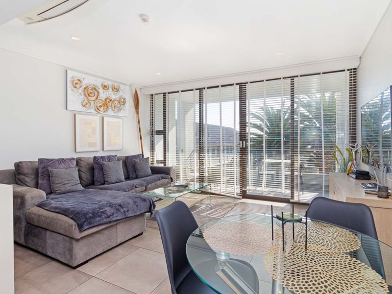 Bright open-plan living and dining area featuring tiled floors, recessed lighting, and large sliding glass doors leading to a balcony.
