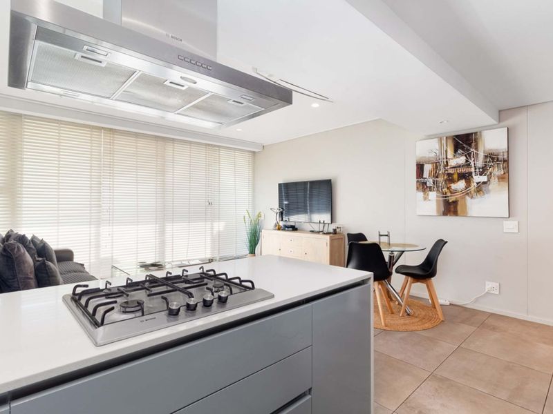 Modern open-plan living area featuring a sleek kitchen island with a gas cooktop, stainless steel extractor fan, and neutral tiled flooring throughout.