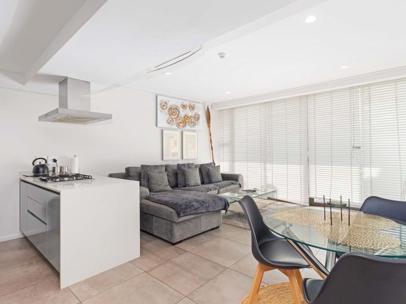 Modern open-plan living area featuring a sleek kitchen island with gas cooktop, tiled flooring, and large windows with venetian blinds.