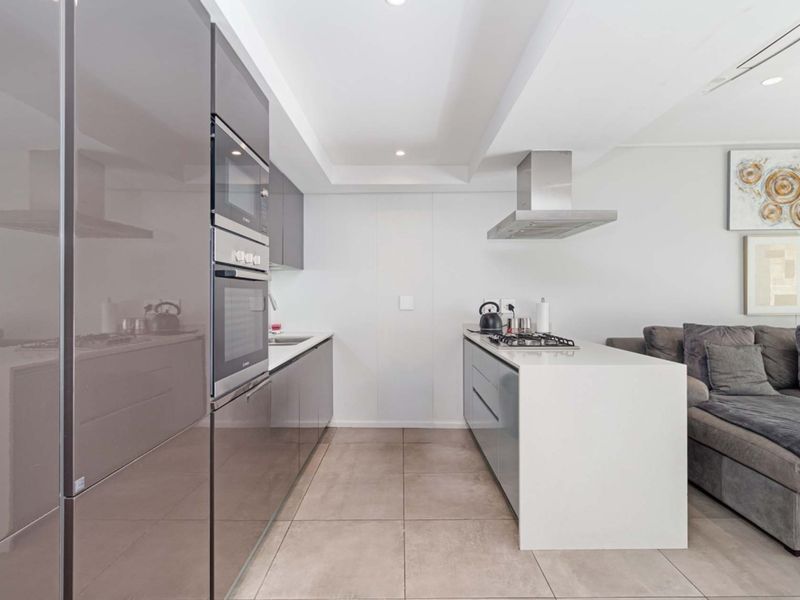 Modern open-plan kitchen featuring sleek cabinetry, integrated appliances, a central island with a gas cooktop, and neutral tiled flooring.