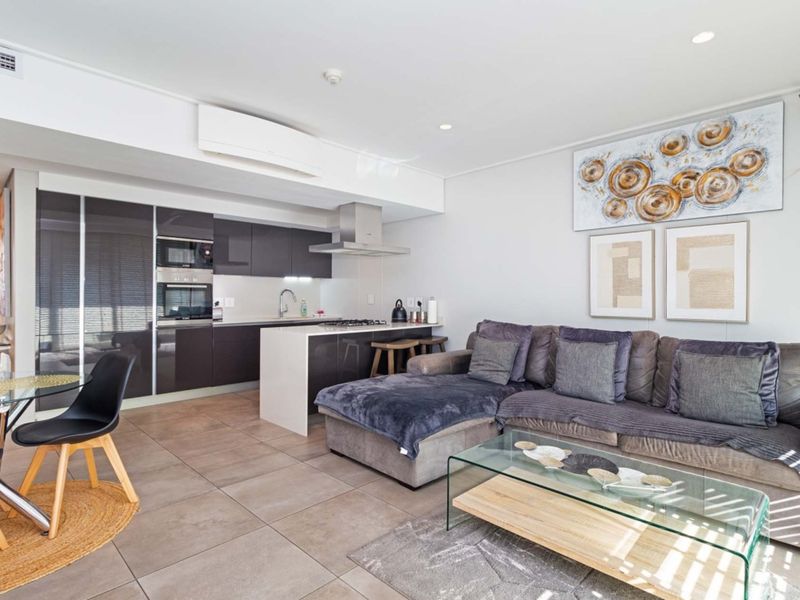 Modern open-plan living area featuring a sleek kitchen with integrated appliances, a central island, and neutral tiled flooring throughout.