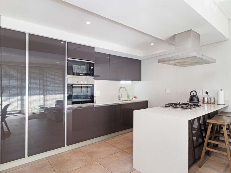 Modern kitchen featuring high-gloss cabinetry, stone countertops, integrated oven and microwave, and a gas hob on a breakfast island.