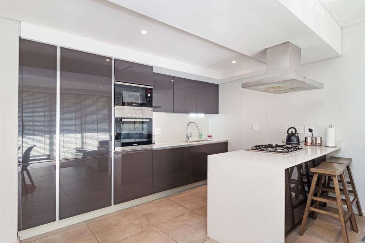 Modern kitchen featuring high-gloss cabinetry, stone countertops, integrated oven and microwave, and a gas hob on a breakfast island.