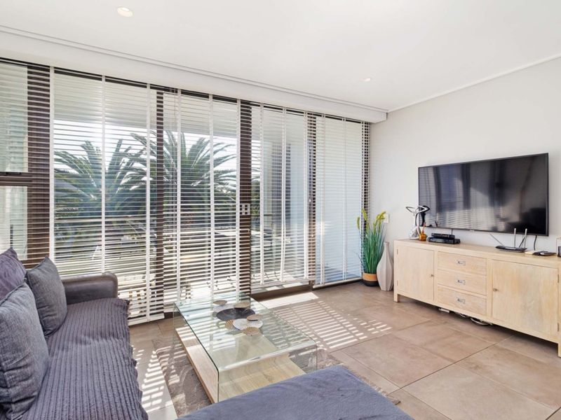 Bright living room featuring large sliding glass doors with venetian blinds, tiled flooring, and recessed downlighting, offering a clean and modern aesthetic.