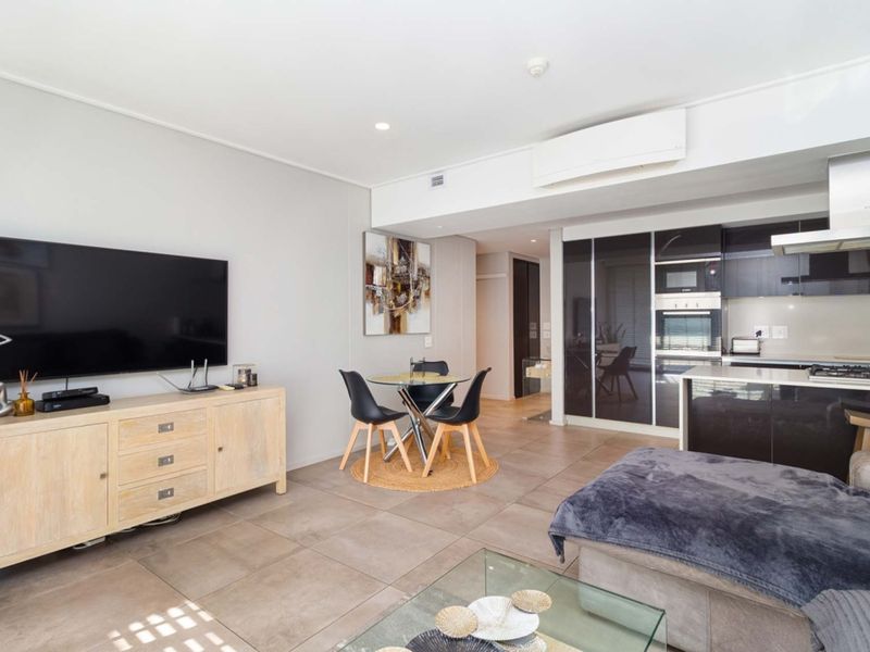 Modern open-plan living area featuring a sleek kitchen with built-in appliances, tiled flooring, and a wall-mounted air conditioning unit.
