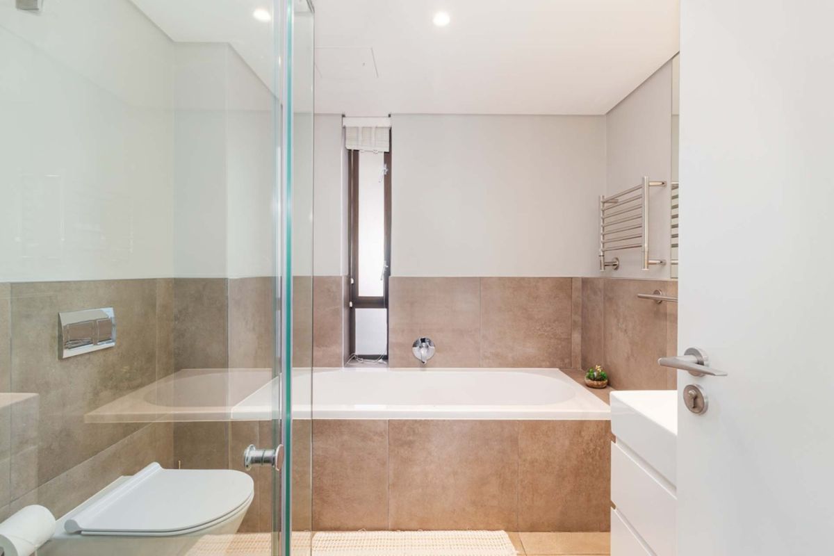 Modern bathroom featuring a built-in bathtub, glass-enclosed shower, wall-mounted toilet, and a heated towel rail with neutral tiled finishes.