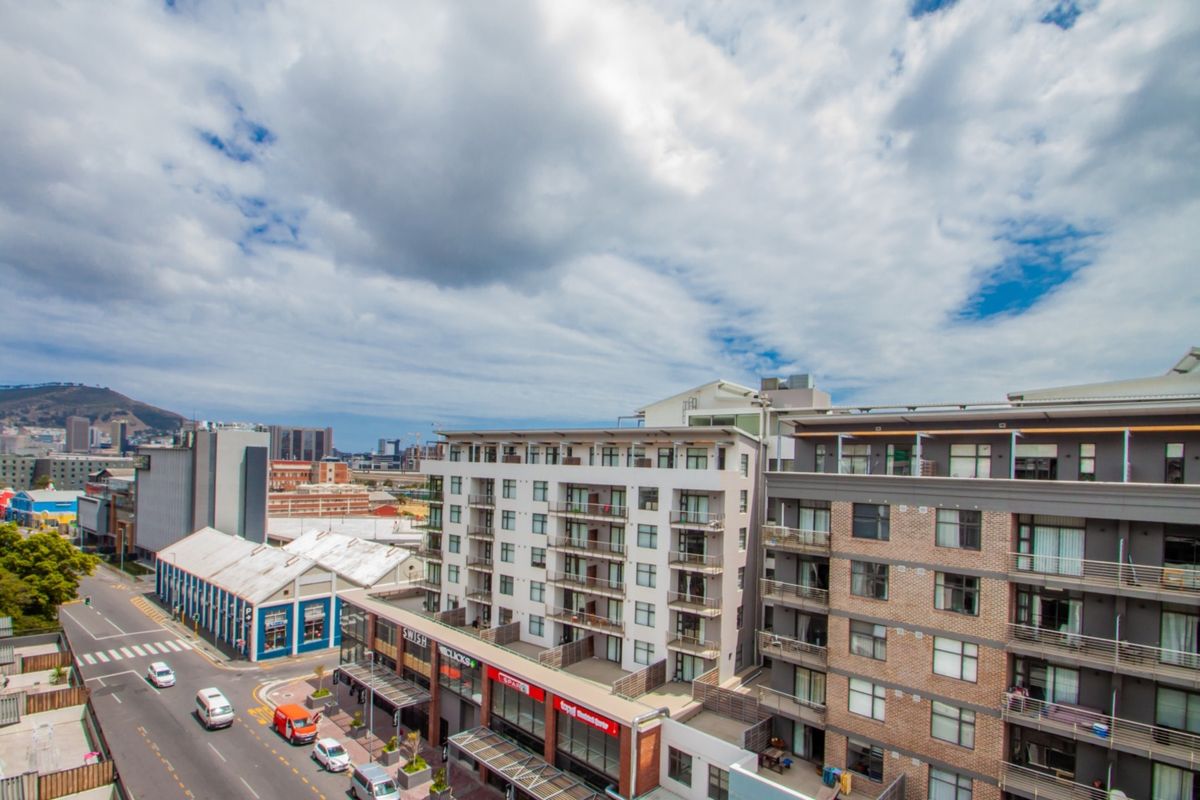 Aerial view of a multi-story apartment complex featuring balconies and ground-floor commercial space, situated in an urban neighborhood setting.