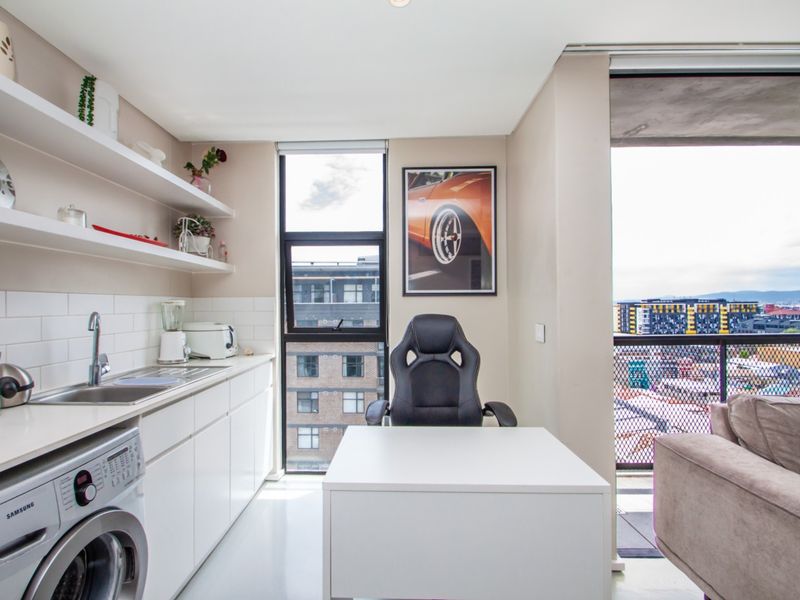Modern open-plan apartment space featuring a compact kitchenette with built-in cabinetry, subway tile backsplash, and direct access to a private balcony.