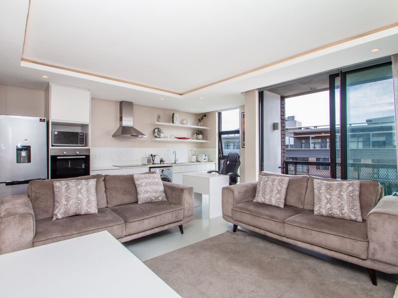 Modern open-plan living area featuring a sleek kitchen with built-in appliances and seamless access to a private balcony through large sliding glass doors.