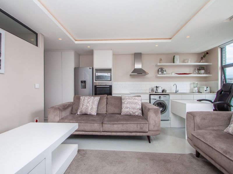 Modern open-plan living area featuring a sleek kitchen with built-in appliances, subway tile backsplash, and recessed ceiling lighting, seamlessly integrated with the lounge space.