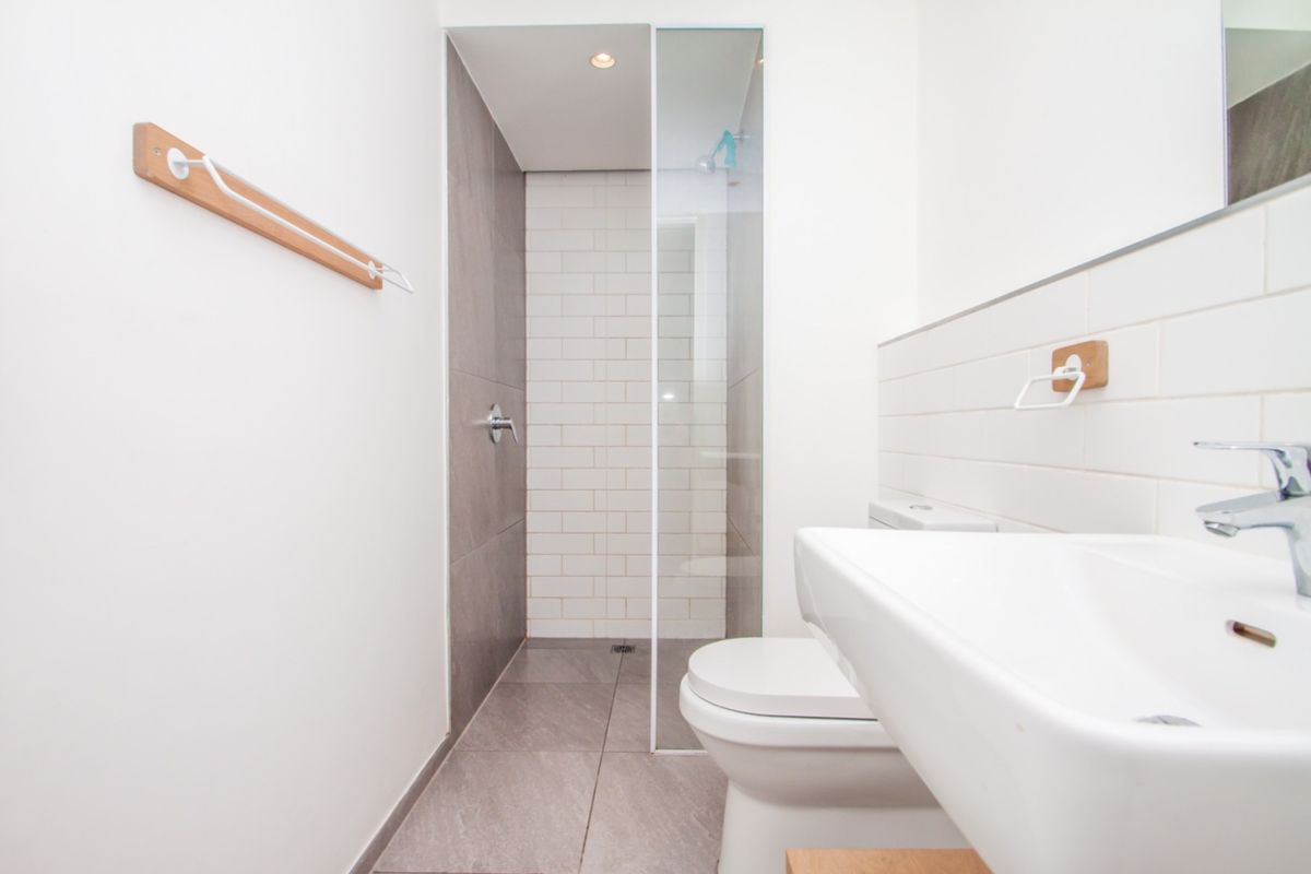 Modern bathroom featuring a walk-in shower with subway tiling, glass screen, wall-mounted basin, and toilet with neutral floor tiles.