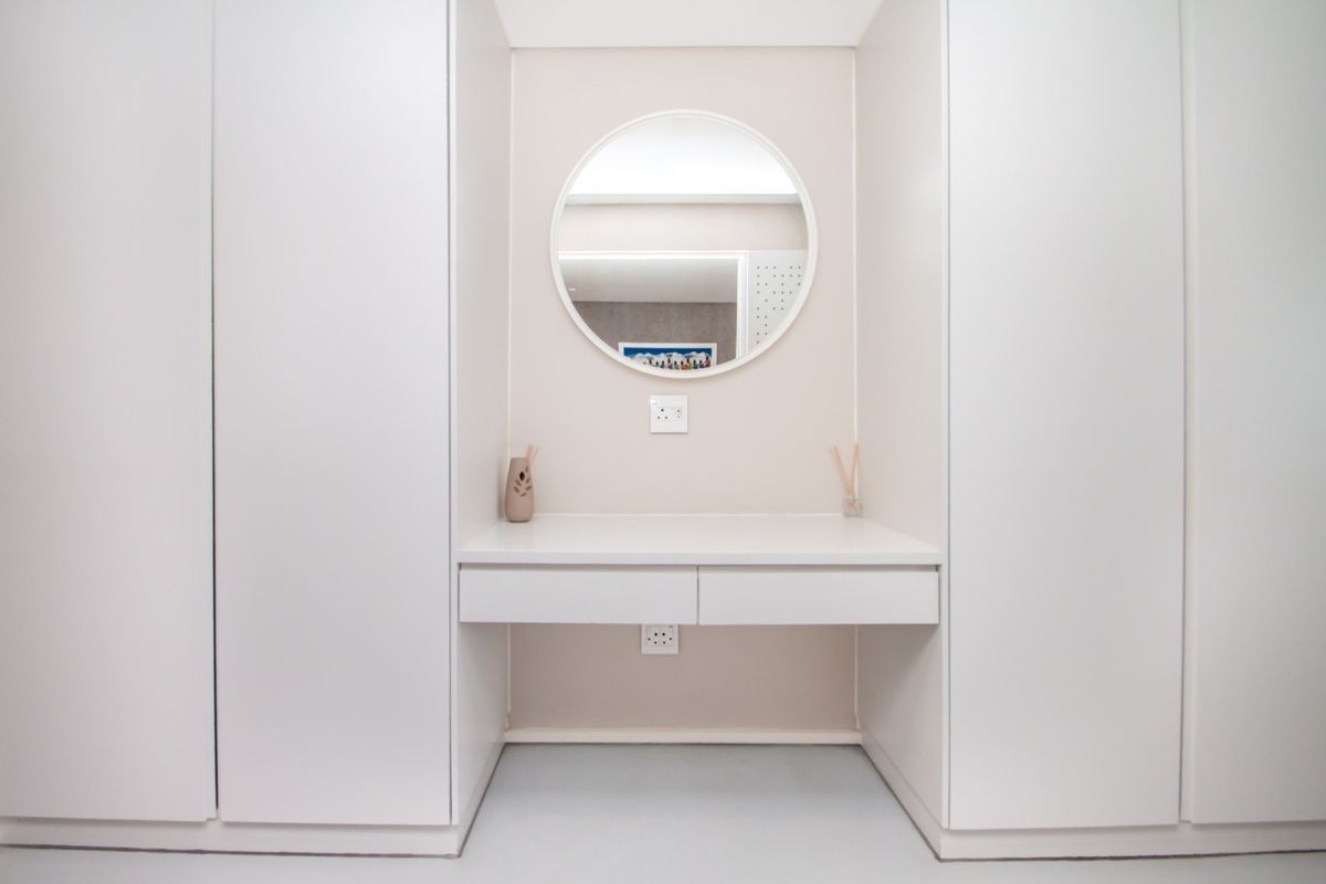 A clean, modern bedroom featuring built-in cupboards and a minimalist vanity desk with a circular mirror.