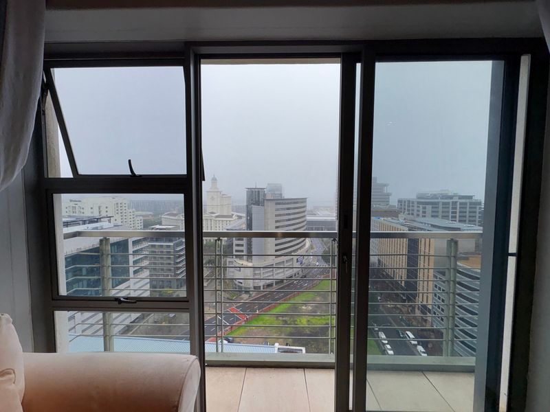 An elevated urban view from an apartment balcony featuring modern aluminium-framed sliding doors and a metal safety railing overlooking the city skyline.