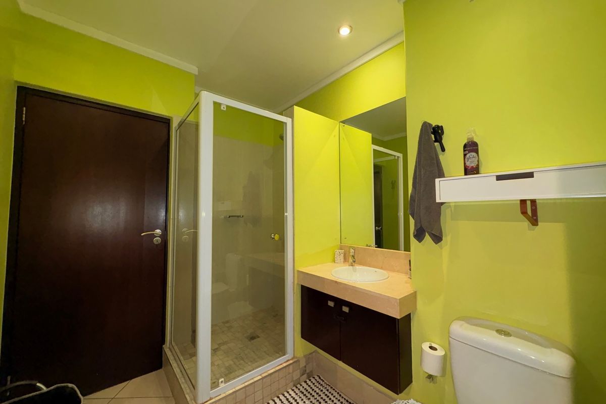 A functional bathroom featuring a shower enclosure, vanity with integrated sink, and toilet, finished with bright wall paint and tiled flooring.