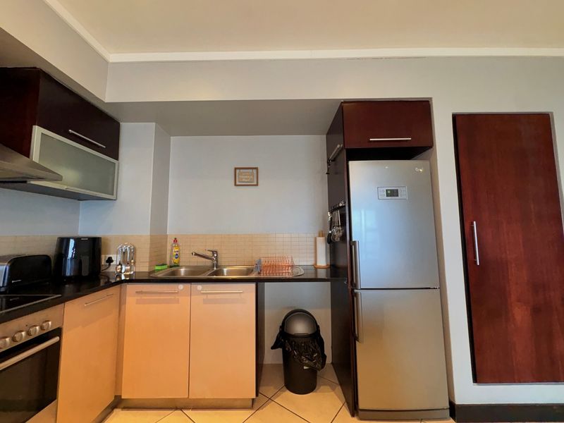 A functional kitchen featuring dark and light wood cabinetry, stone countertops, a stainless steel sink, and integrated appliances including an oven and extractor fan.