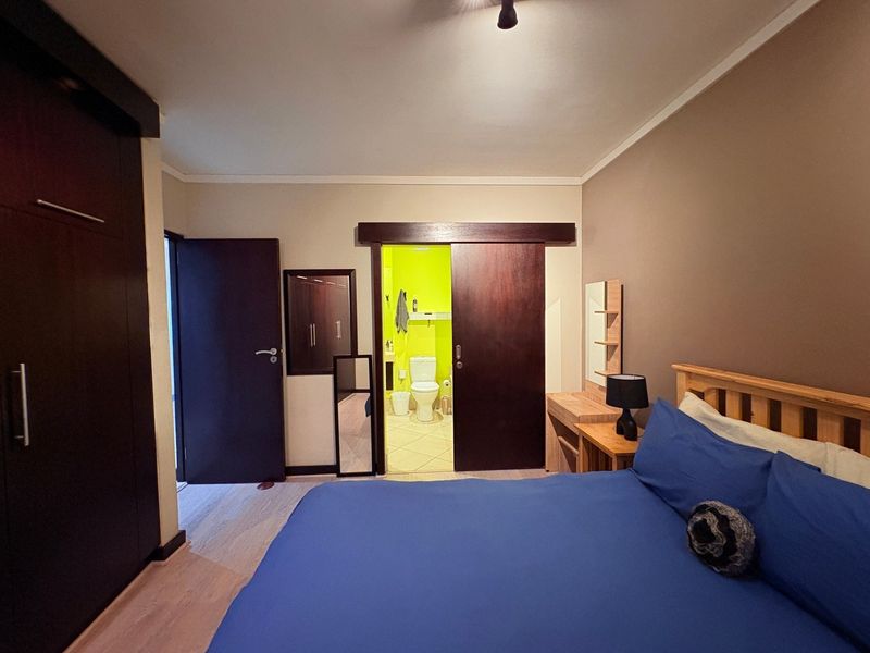 Bedroom featuring laminate flooring, a large built-in wardrobe, and a sliding door providing direct access to an en-suite bathroom.