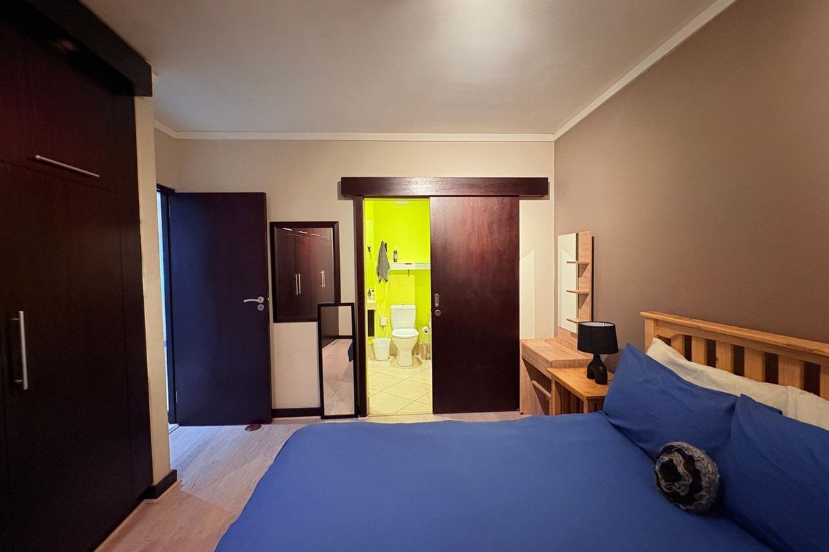 Bedroom featuring laminate flooring, a large built-in wardrobe, and a sliding door providing direct access to an en-suite bathroom.