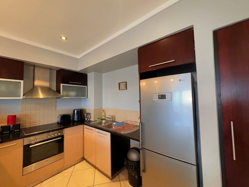 A functional kitchen featuring dark wood cabinetry, granite countertops, a stainless steel oven, hob, and extractor fan with tiled backsplash and neutral floor tiles.